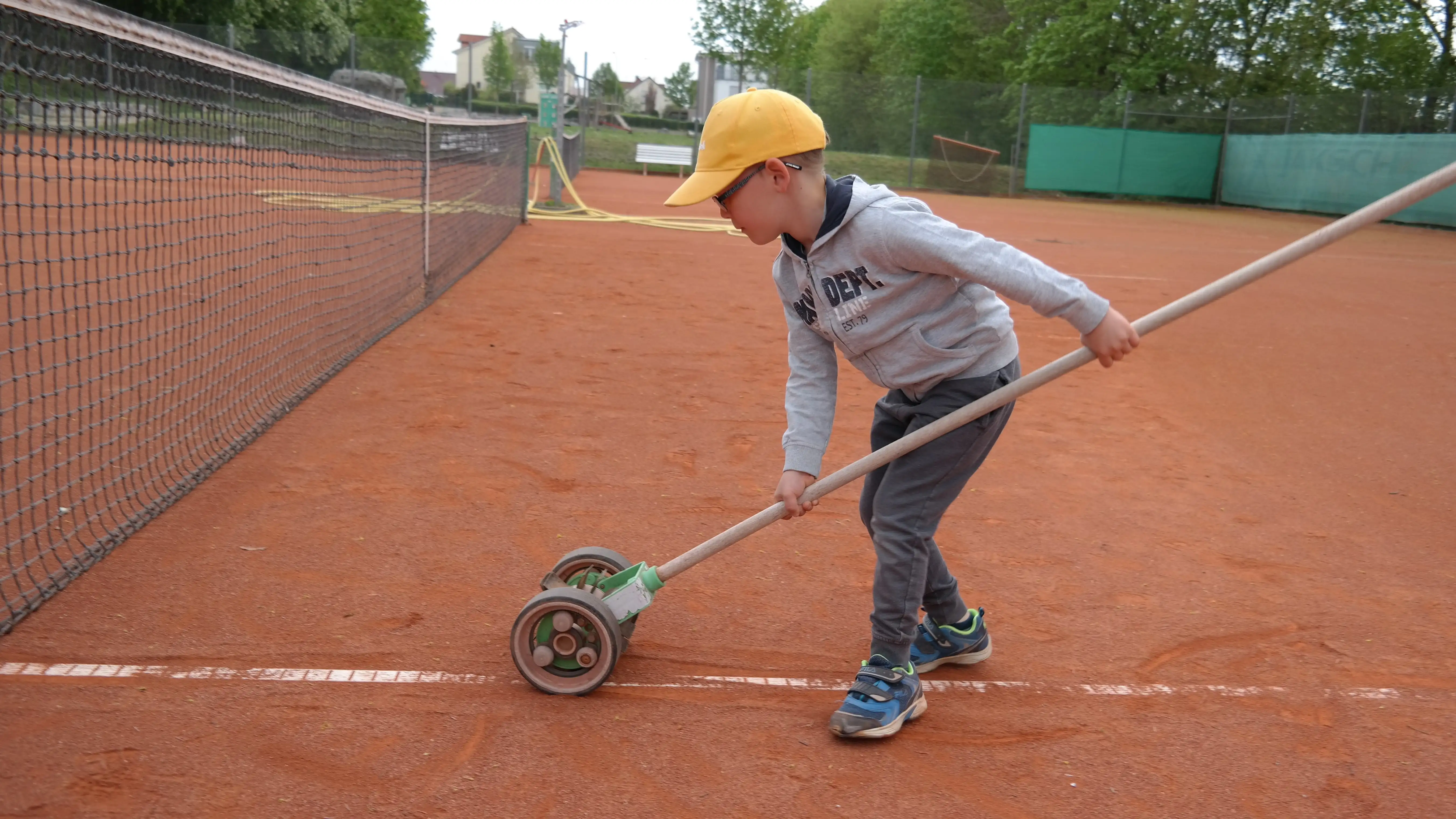Kind pflegt Tennisplatz nach Training